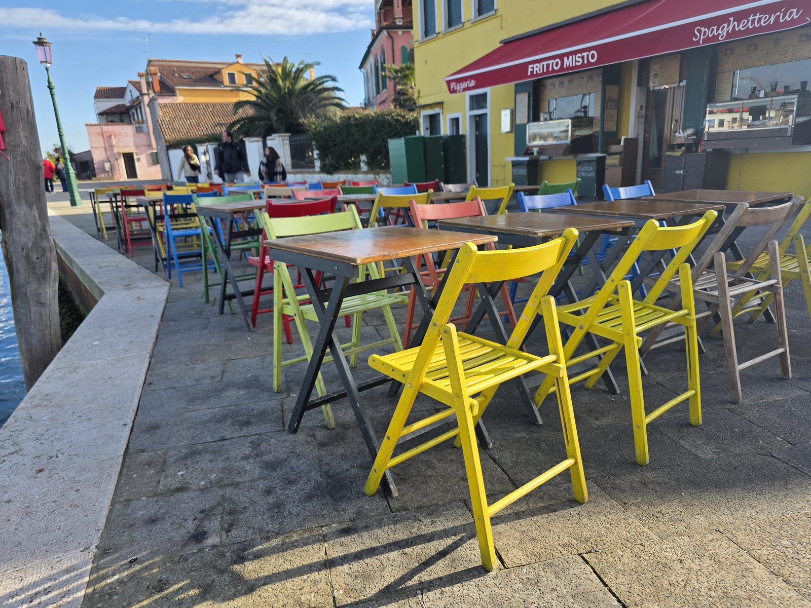Bunte Klappstühle eines Lokals direkt am Kanal von Burano