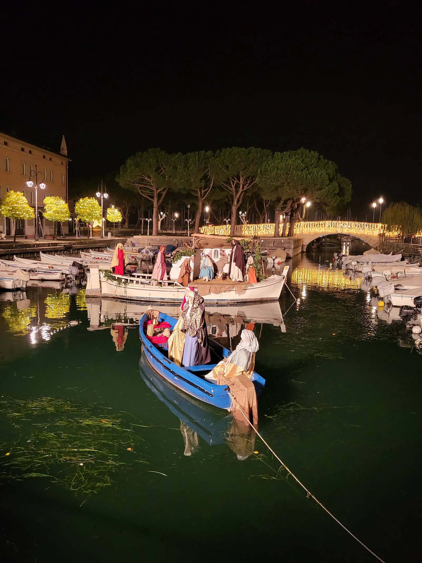 Beleuchtete Weihnachtskrippe auf Booten im alten Hafen von Desenzano